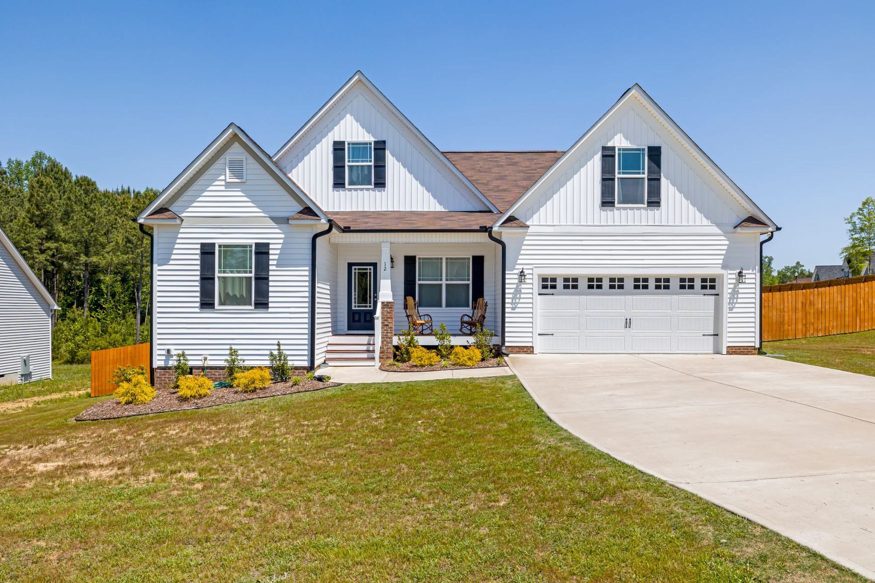 White two-story suburban home with a covered front porch, double garage, and a green front lawn under a blue sky